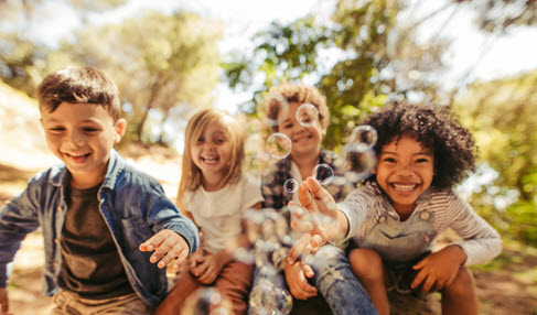 Vier Kinder schauen lachend in die Kamera und spielen mit Seifenblasen.