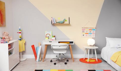 In einem Kinderzimmer steht ein Schreibtisch mit einem Schreibtischstuhl auf Rollen.