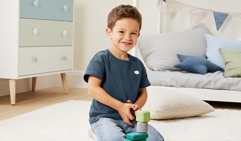 Ein Zimmer zum Träumen: Ein kleiner Junge hockt auf dem Boden seines Kinderzimmers und spielt mit Spielzeugen.