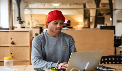 Junger Mann sitzt in Sweatshirt in einem Café an seinem Laptop und arbeitet.