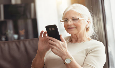 Seniorin mit einem Handy in der Hand.