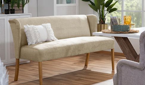 Unglaublich haltbar: Ein beiges Küchensofa mit einem weißen Kissen steht am Ende einer großen Tafel. Der Samtstoff verhindert Kratzer und Flecken.
