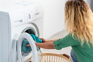 Eine Frau legt ihr grünes Sweatshirt in die Waschmaschine.