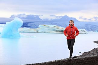 Ein Mann geht mit seiner roten Outdoorjacke an einem See laufen.