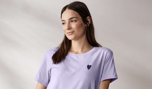 Eine junge Frau trägt ein lila T-Shirt mit kurzen Ärmeln und einem schwarzen Herz als Aufdruck.