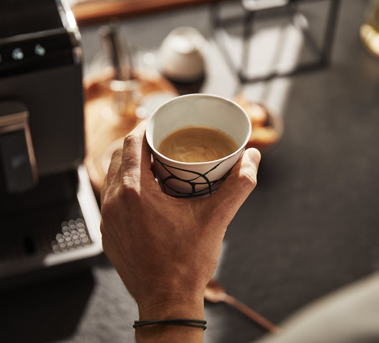 Mann hält Kaffeetasse mit einem Caffè Crema vor einem Kaffeevollautomaten