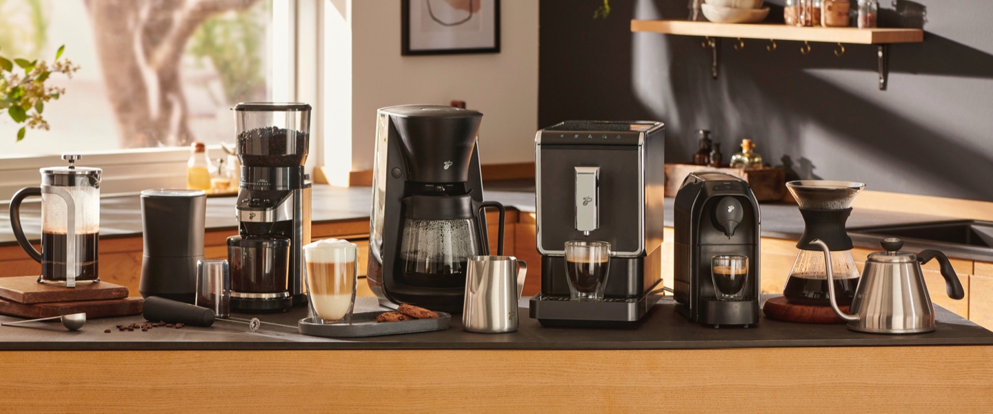 Ein stimmungsvolles Bild einer lachenden Frau, die ihren Kaffee zubereitet leitet den Einstieg auf die Kaffeemaschinen und -bereiter Seite ein. Entdecken Sie hier für jede Zubereitungsart die passende Maschine.