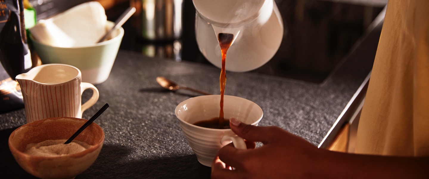 Stimmungsvolles Bild, in dem Kaffee aus einer Kanne in eine Tasse eingeschenkt wird.