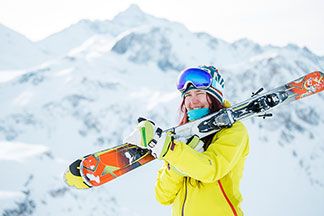 Eine Frau mit einer gelben Ski Jacke trägt ihre Ski.