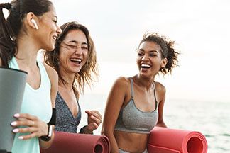 Drei Frauen gehen mit ihren Sport Tops zum Sport und lachen dabei.