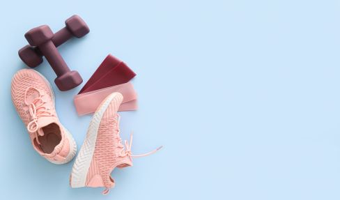 Dem Trend folgen: Auf dem Boden liegen hellrosa Sportschuhe, Gewichte und Haarbänder.