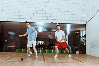 Zwei Männer spielen in ihren Sportshirts Squash in einer Halle.