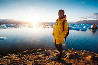 Eine Frau steht mit ihrer gelben Outdoorjacke an einem Berg See.