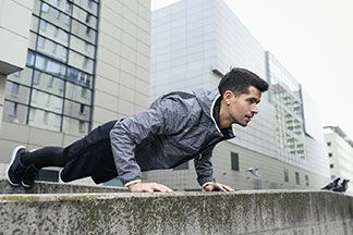 Ein Mann trägt eine Outdoorjacke mit Kapuze und macht Liegestütz.