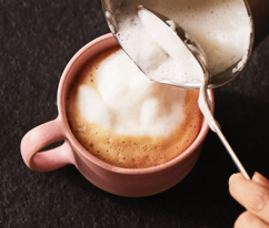 Milchschaum wird auf einen Tasse Kaffee mit einem Löffel gegeben