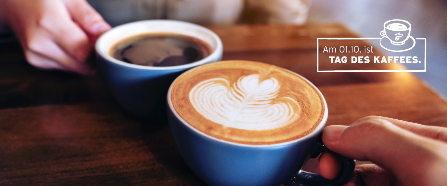 Zwei Kaffeetassen stoßen an, was auf den Tag des Kaffees verweist.
