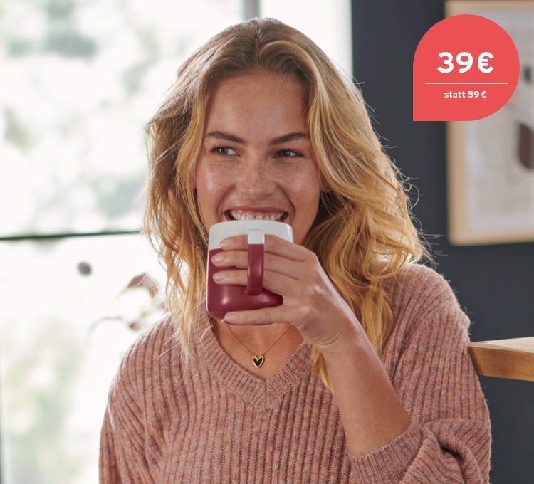 Eine Frau trinkt genüsslich ihren Kaffee aus einer Filterkaffeemaschine, die im Hintergrund zusehen ist.