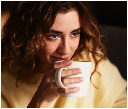 Brünette Frau trinkt setzt eine weiße Kaffeetasse an die Lippen zum trinken an