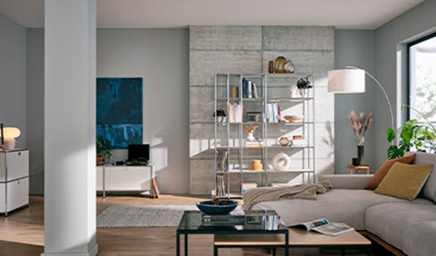 Zeitlose Möbel: In einem klassisch eingerichteten Wohnzimmer steht ein hellgraues Sofa und ein großes Regal.