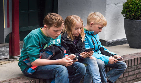 Drei Kinder sitzen mit ihren Handys in der Hand auf einer Mauer.