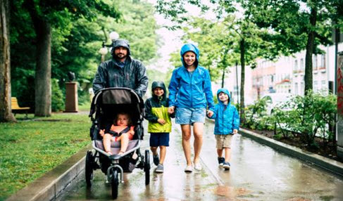 Großartige Qualität: Eine Familie macht in Regenjacken in verschiedenen Farben eine Spaziergang durch den Regen.