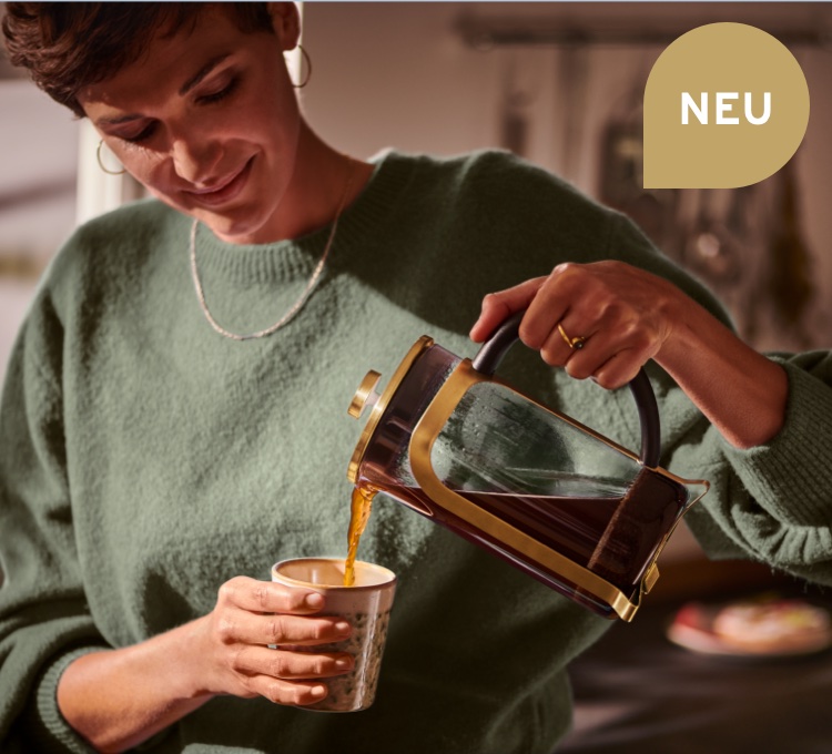 Frau gießt mit der goldenen Siebstempelkanne ihren Kaffee in eine Tasse.